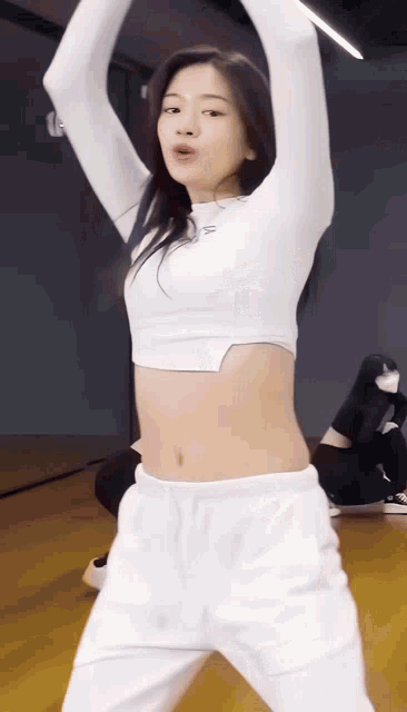 a woman in a white crop top and white sweatpants is dancing in front of a mirror