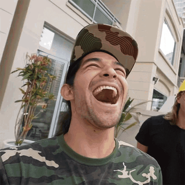 a man wearing a camouflage shirt and a hat is laughing