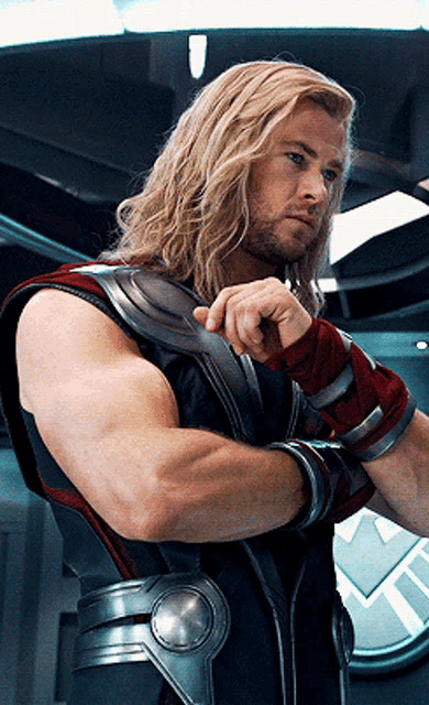 a man with long blonde hair and a beard is standing in front of a shield logo
