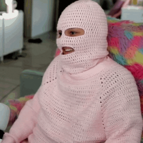 a woman wearing a ski mask and a pink sweater is sitting on a chair .