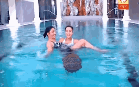 two women are swimming in a pool with a banner that says abp on it