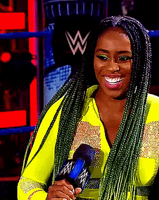 a woman with green braids is smiling while holding a microphone with the letter w on it .
