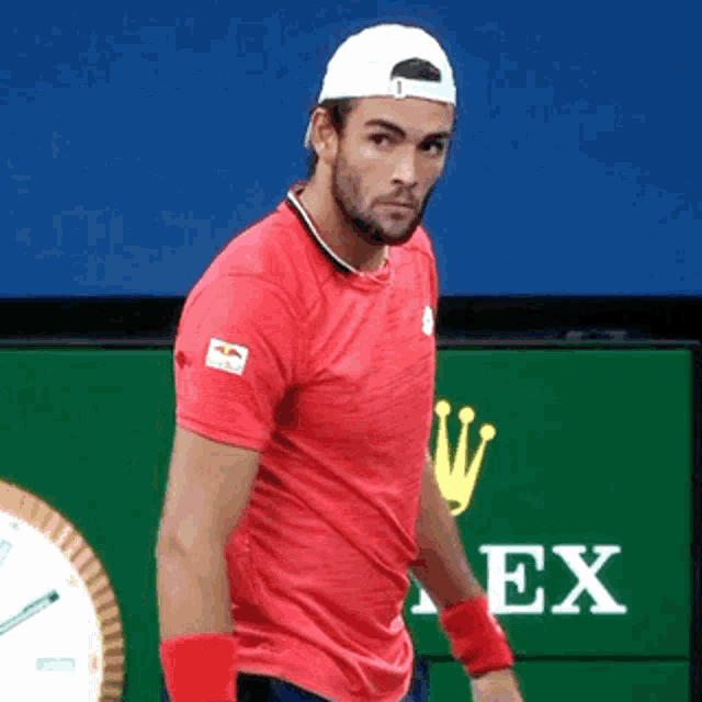 a man in a red shirt is standing in front of a rolex logo