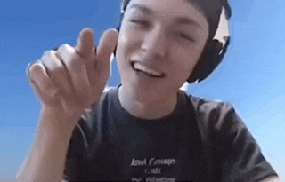 a young man wearing headphones and a black shirt is smiling and giving a thumbs up .