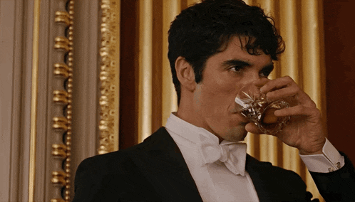 a man in a tuxedo drinks from a glass