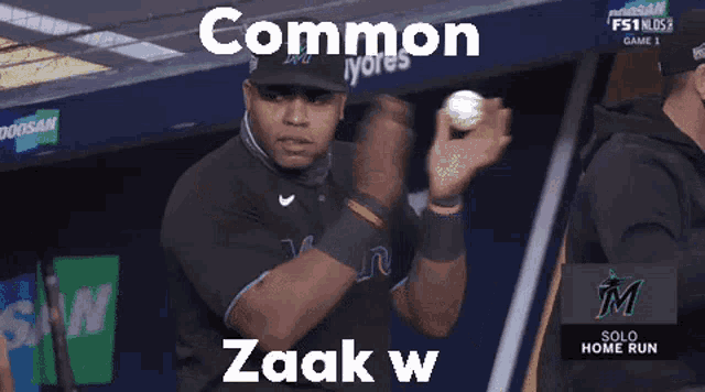 a man in a baseball uniform holds a ball in his hand and says " common zaak w "
