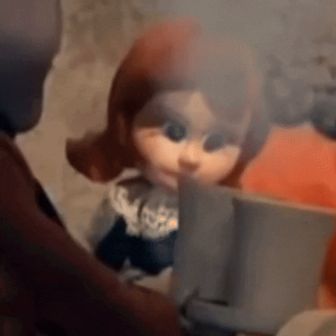 a close up of a doll with red hair looking at a book .