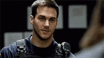 a man with a beard and a microphone on his shoulder is standing in a dark room .