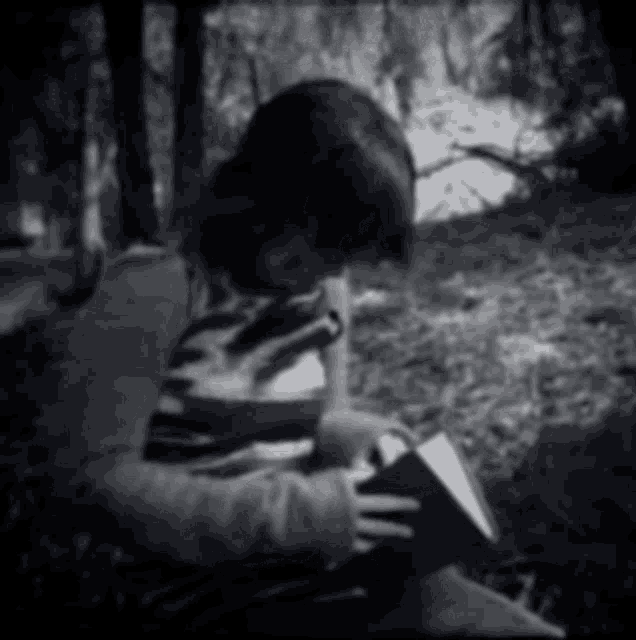 a person reading a book in the woods with trees in the background