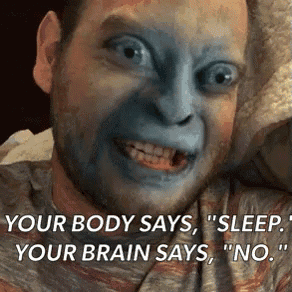a man with blue paint on his face is making a funny face while laying in bed .