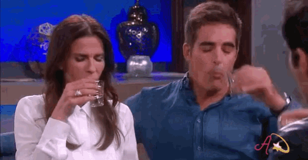 a man and a woman are drinking from a glass while sitting next to each other .