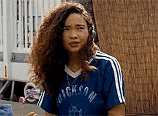 a woman with curly hair is wearing a blue shirt with white stripes and a necklace .