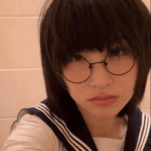 a girl wearing glasses and a sailor suit looks at the camera