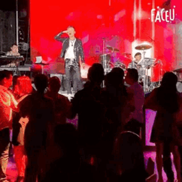 a man is singing into a microphone on a stage in front of a crowd of people .