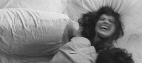 a black and white photo of a man and a woman laying in bed laughing .