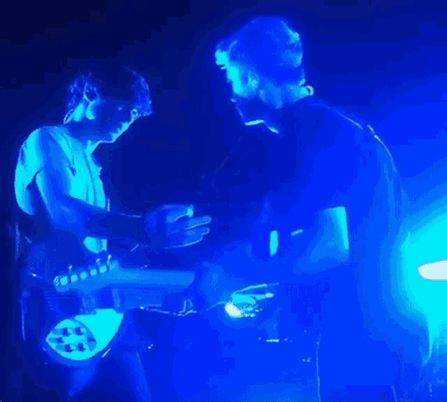 a man is playing a guitar in a dark room with blue lights behind him .