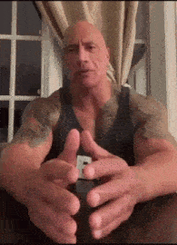 a man with a lot of muscles is sitting at a table with his hands folded in front of a window .