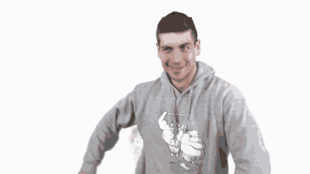 a man wearing a grey hoodie with a cartoon character on it saluting