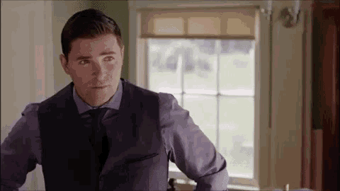 a man in a suit and tie is standing in front of a window in a living room .