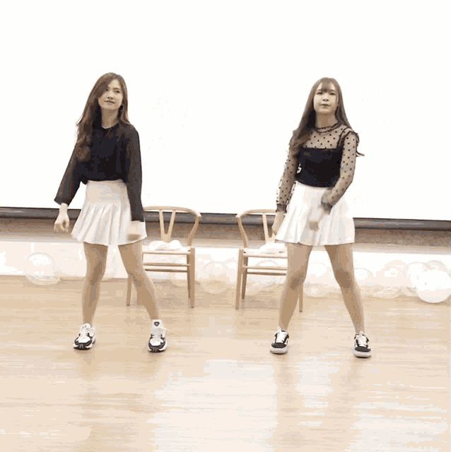 two girls in white skirts are dancing in front of chairs