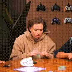 a woman in a brown hoodie is sitting at a table playing a video game