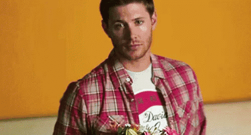 a man in a plaid shirt is holding a bouquet of flowers in front of his face .