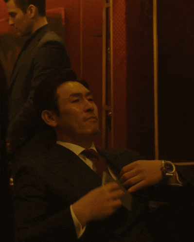 a man in a suit adjusts his tie while another man stands behind him