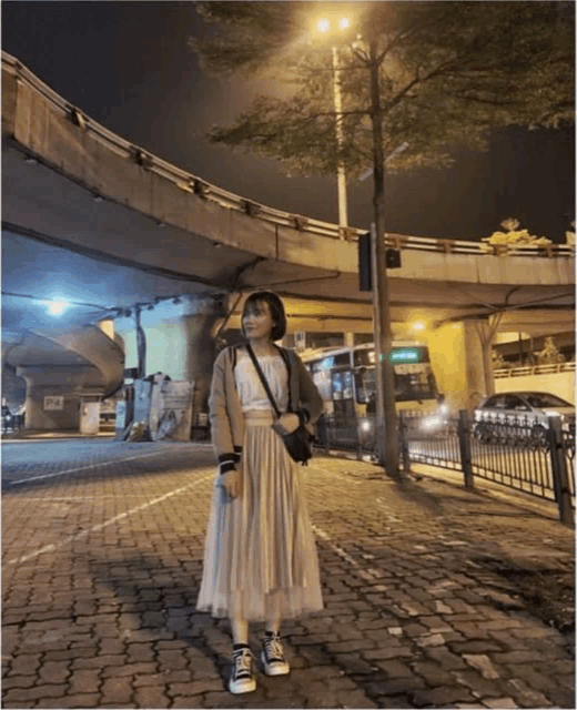 a woman standing under a bridge with a bus that says ' hong kong ' on it