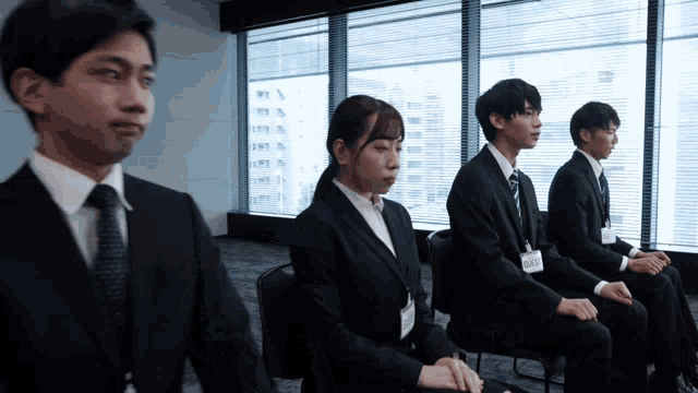 a group of people in suits and ties are sitting in front of a window and one of them has a name tag that says yuki
