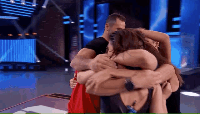 a group of people are hugging each other on a stage and one of them is wearing a red shirt