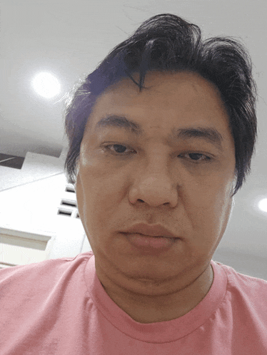 a man in a pink shirt looks at the camera with a serious look on his face