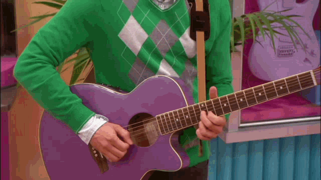 a man in a green sweater plays a purple guitar in front of a display of guitars