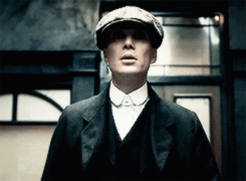 a man wearing a hat and a suit stands in front of a building