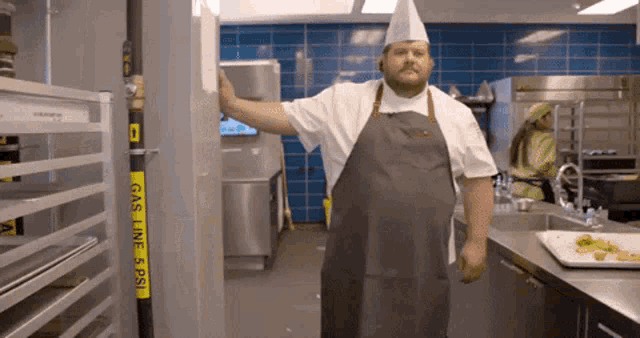 a man in an apron stands in a kitchen next to a gas line 5 psi sign