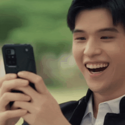 a man in a suit is laughing while looking at his phone