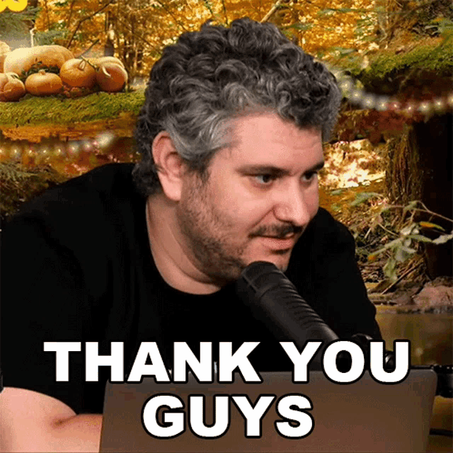 a man sitting in front of a microphone with the words thank you guys behind him