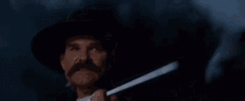 a man with a hat and mustache is holding a gun in his hand and saying `` hell 's coming with me '' .