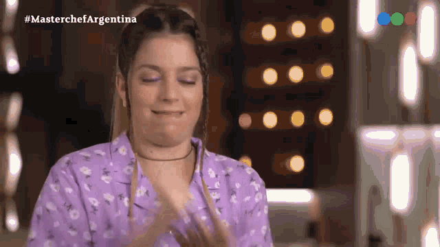 a woman in a purple shirt applauds in front of a screen that says #masterchefargentina