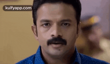 a man with a mustache and a blue shirt is talking to someone .