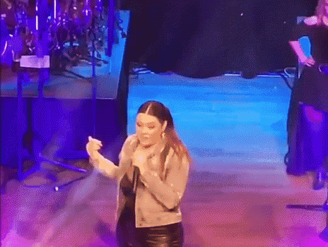 a woman is singing into a microphone on a stage while dancing .