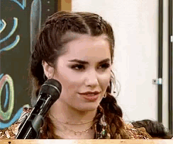 a woman is speaking into a microphone in front of a chalkboard with the number 0 on it