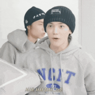 a man wearing a hoodie that says nct stands next to another man wearing a beanie