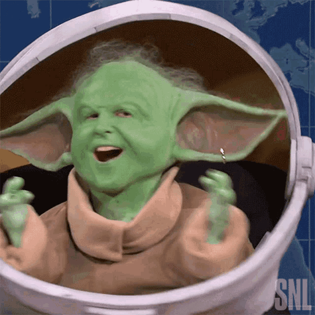 a person dressed as a baby yoda in a helmet with snl written on it