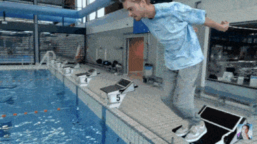 a man in a blue shirt is jumping off a starting block in a swimming pool
