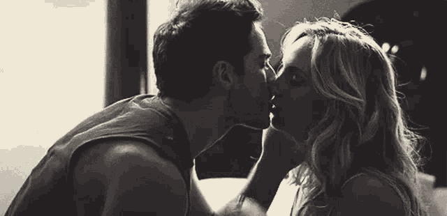 a black and white photo of a man and a woman kissing .