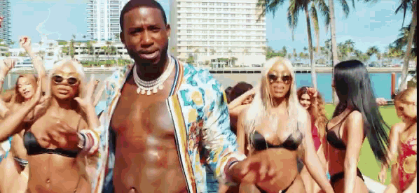 a man without a shirt is standing in front of a group of bikini clad women .
