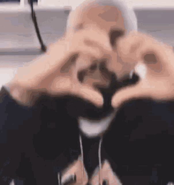 a person is making a heart shape with their hands in front of their face .
