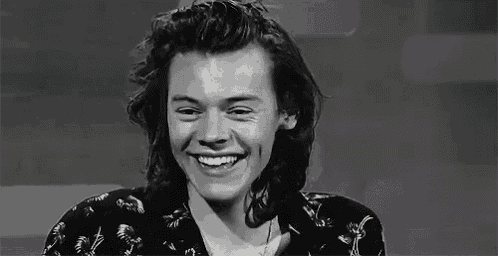 a black and white photo of harry styles laughing with his eyes closed .