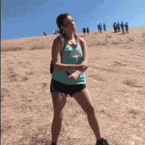 a woman in a green tank top and black shorts is standing on top of a dirt hill .