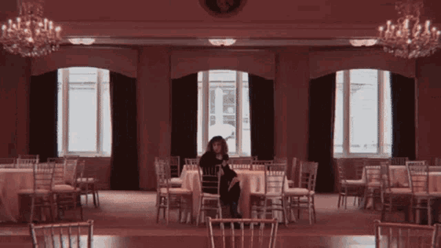 a woman sits at a table in an empty room with tables and chairs